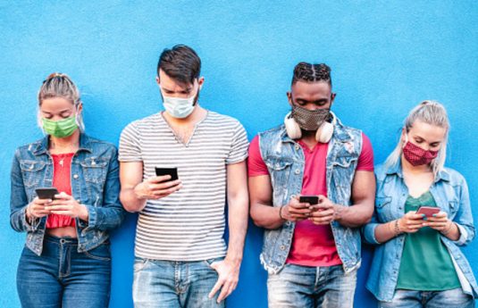 Multiracial friends with face masks using tracking app with mobile smart phones - Young millenial people sharing content on social media networks - New normal lifestyle concept - Bright vivid filter