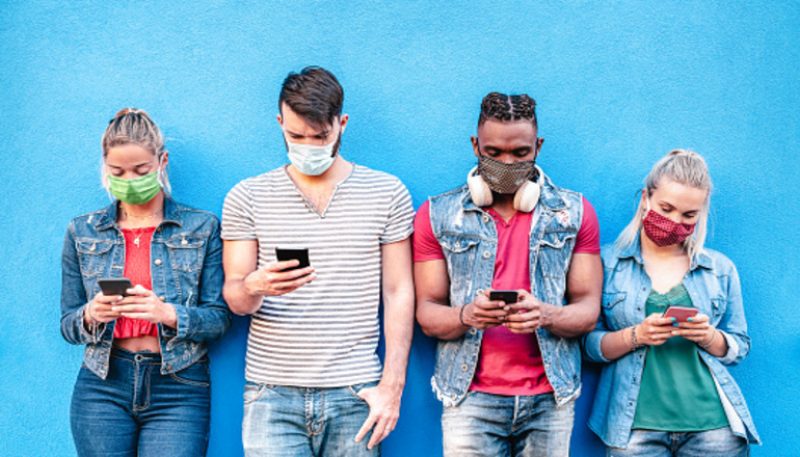 Multiracial friends with face masks using tracking app with mobile smart phones - Young millenial people sharing content on social media networks - New normal lifestyle concept - Bright vivid filter